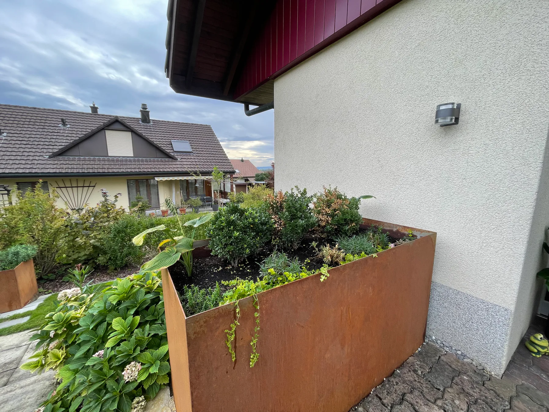 Hoches bepflanztes Stahlbeet mit rostfarbener Oberfläche neben einer Hausfassade